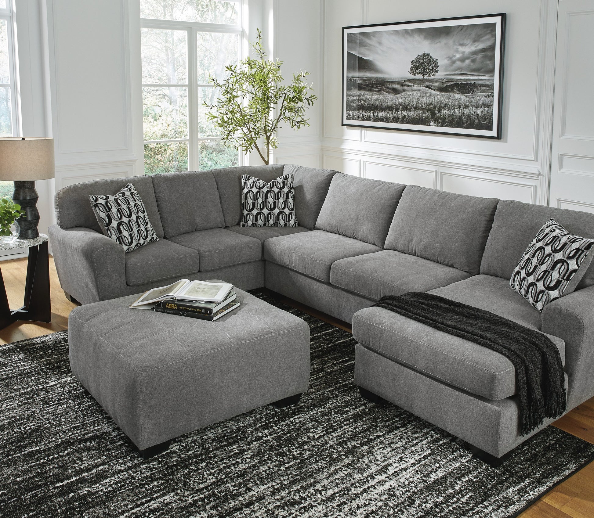 Ashley 324-02 sectional with ottoman from Moda Home Furniture, featuring modern gray upholstery and plush cushions, ideal for lounging and entertaining guests.